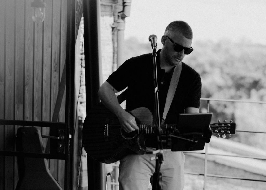 Man playing guitar on a wooden deck with scenic background